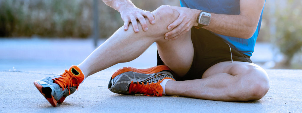 Homme qui se tient la jambe avec les deux mains, assit sur le sol. 